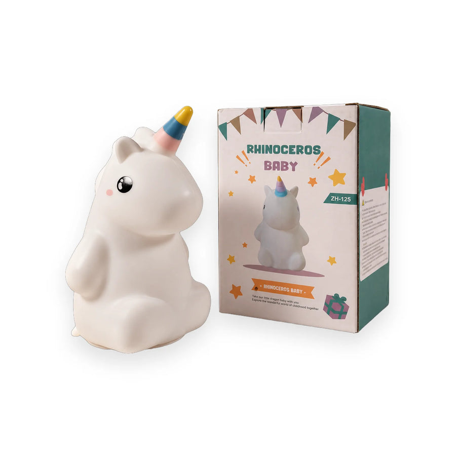 White Rhinoceros Baby unicorn toy with a rainbow horn, sitting on a glittery surface beside its packaging